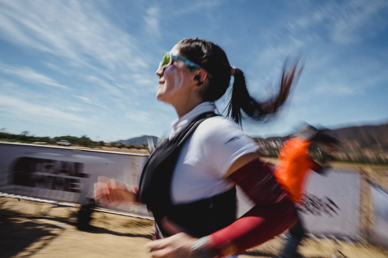 A runner smiling, hair flying, a Trail & Wine banner blurred behind her.