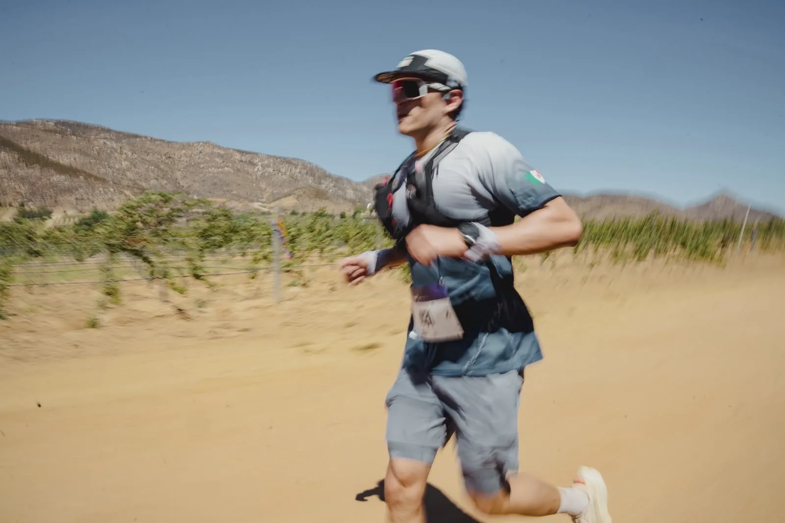 A trail runner mid-stride, motion-blurred, vineyard and mountains behind.