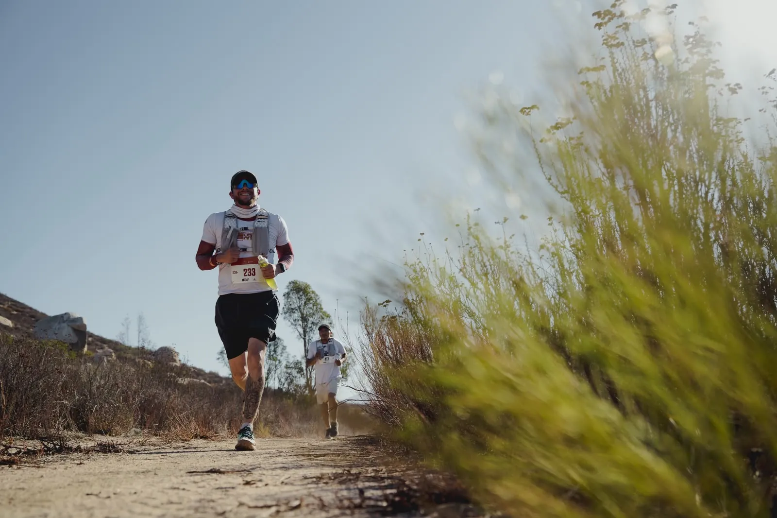 A runner smiling on the climb, wildflowers in the foreground.