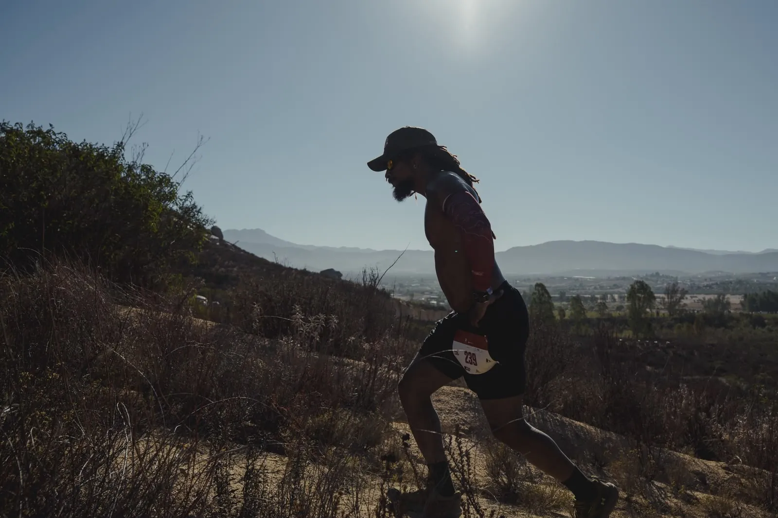 A runner silhouetted against the sun, climbing a steep hill.