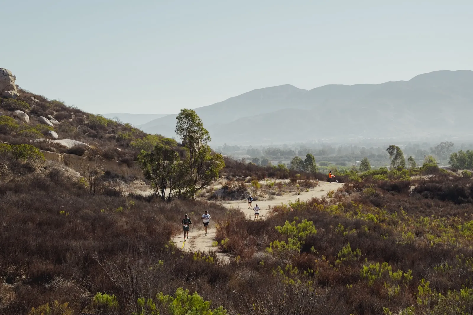 Runners descending a hillside trail into a hazy valley view.